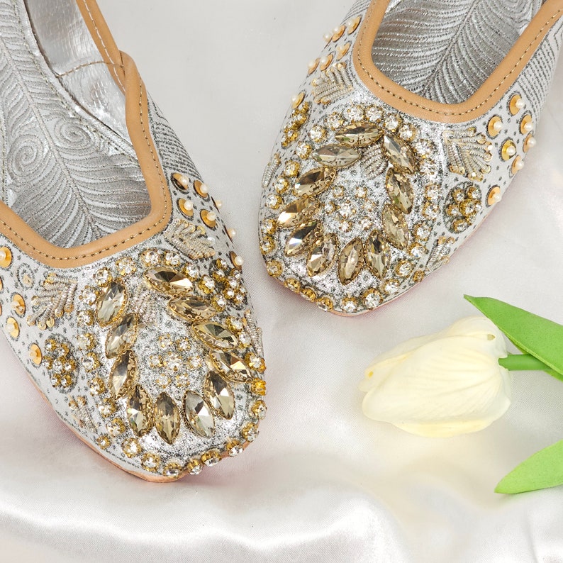 Peut inclure: Une paire de chaussures plates argent&eacute;es et dor&eacute;es orn&eacute;es d'une pointe pointue. Les chaussures sont d&eacute;cor&eacute;es de strass et ont une doublure en cuir beige.