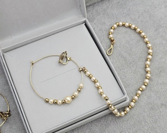 May include: Gold-tone hoop earrings with faux pearls and gold beads. The earrings are in a white box with a gray interior. A matching pearl and gold bead necklace is also visible.