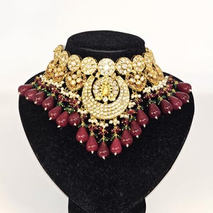Pu&ograve; includere: Una collana in oro e argento con un grande ciondolo decorato e una frangia di perline rosse e verdi.
