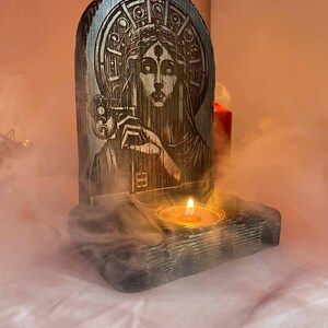 以下が含まれることがあります： 3つ目の女性と鍵の彫刻が施された木製キャンドルホルダー。キャンドルホルダーの中央には小さなキャンドルがあります。