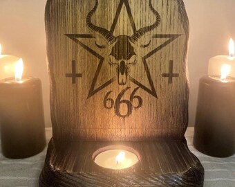 May include: A wooden candle holder with a pentagram design, a goat skull, and the number 666. The candle holder is brown with a distressed finish and has a small round opening to hold a tea light candle. Several lit candles surround the holder.