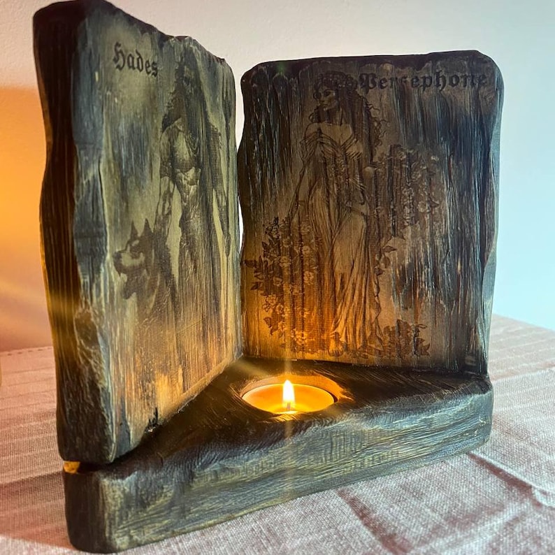 Może przedstawiać: Drewniany świecznik z rzeźbą Hadesa i Persefony. Świecznik ma miejsce na świeczkę typu tealight w środku.