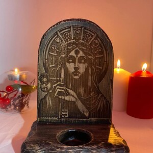以下が含まれることがあります： 王冠と第三の目をつけた女性の彫刻が施された木製キャンドルホルダー。ホルダーはダークウッド仕上げで、底にキャンドルホルダーが1つあります。