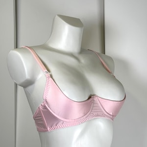 Op de afbeelding: Een lichtroze beha met beugel, getoond op een witte mannequin. De beha heeft verstelbare bandjes en een satijnen afwerking. Het ontwerp heeft een geschulpte rand aan de onderkant.