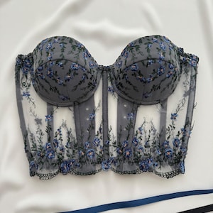 Peut inclure: Un corset en dentelle noire et bleue &agrave; fleurs avec une structure &agrave; baleines et un d&eacute;collet&eacute; en c&oelig;ur.