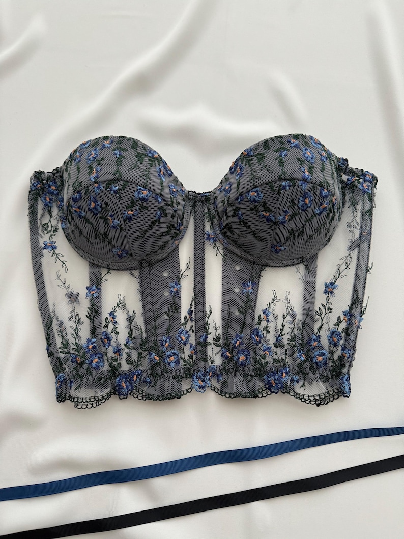 Peut inclure: Un corset en dentelle noire et bleue &agrave; fleurs avec une structure &agrave; baleines et un d&eacute;collet&eacute; en c&oelig;ur.
