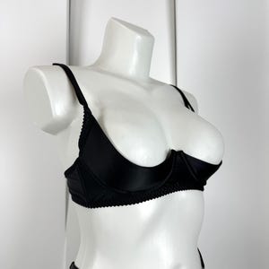 May include: A black bra and matching underwear set displayed on a white mannequin. The bra features underwire support and delicate trim along the edges. The lingerie set is made of a smooth, shiny fabric.