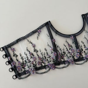 Peut inclure: Tissu noir transparent avec broderie florale violette et bretelles &eacute;lastiques noires. Le tissu a un bord festonn&eacute;.