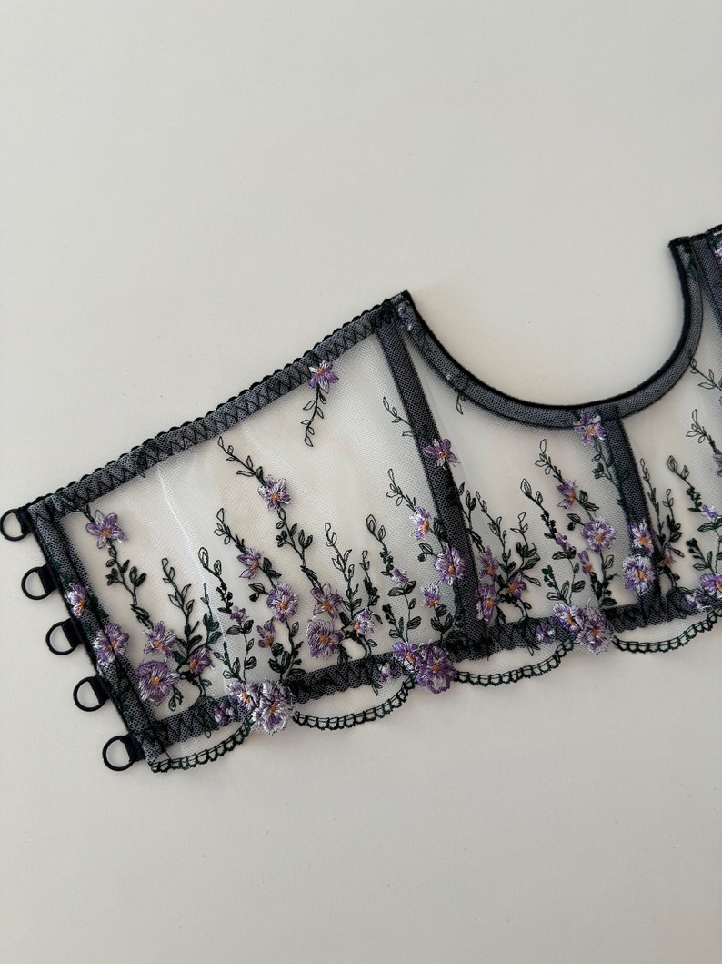 Peut inclure: Tissu noir transparent avec broderie florale violette et bretelles &eacute;lastiques noires. Le tissu a un bord festonn&eacute;.
