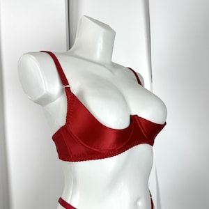 May include: A red satin lingerie set displayed on a white mannequin. The set includes a balconette bra with adjustable straps and a matching thong. The bra features underwire support and delicate stitching. The lingerie is a vibrant shade of red.