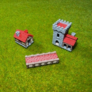 May include: A miniature set featuring a small house with a red roof, a stone-textured castle tower with a red roof, and a rectangular stone wall section with a red brick top. These three painted gaming terrain pieces are arranged on a green surface.