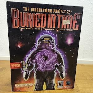 May include: A black box for "The Journeyman Project 2: Buried in Time" video game. The box art features an astronaut figure with purple energy effects against a starry background. The text "The Epic Time Travel Adventure" is also visible.