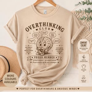 Puede incluir: Una camiseta beige de manga corta con un gráfico marrón de un cerebro de dibujos animados. El texto dice OVERTHINKING CLUB, PROUD MEMBER, e incluye frases como DEEP THOUGHTS, LATE NIGHTS y TOO MANY THOUGHTS + NOT ENOUGH ANSWERS.