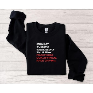 Puede incluir: Sudadera negra de cuello redondo con texto blanco que enumera los d&iacute;as de la semana y t&eacute;rminos relacionados con las carreras. La palabra "Practice" va seguida de un icono de bandera a cuadros roja, y "Race Day" tiene un gr&aacute;fico de coche de carreras rojo.