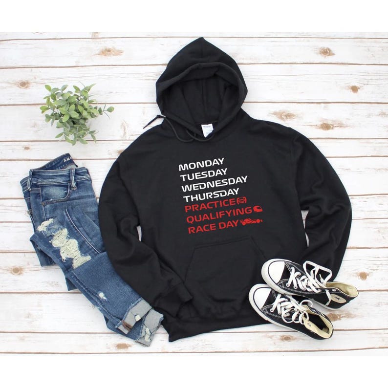 Puede incluir: Sudadera con capucha negra con texto blanco que enumera los d&iacute;as de la semana y los t&eacute;rminos de carreras. La sudadera se combina con vaqueros azules y zapatillas de lona negras con suelas y cordones blancos. Una peque&ntilde;a planta est&aacute; a la izquierda.