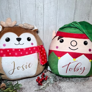 May include: Two plush toys, one a brown reindeer with a red and white scarf and the name "Josie" embroidered on it, and the other a green elf with a red hat and the name "Toby" embroidered on it.