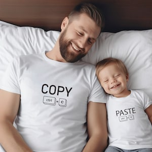 Puede incluir: Una camiseta blanca con el texto "COPY" y el atajo de teclado "ctrl + c" impreso en ella. Una segunda camiseta blanca con el texto "PASTE" y el atajo de teclado "ctrl + v" impreso en ella.