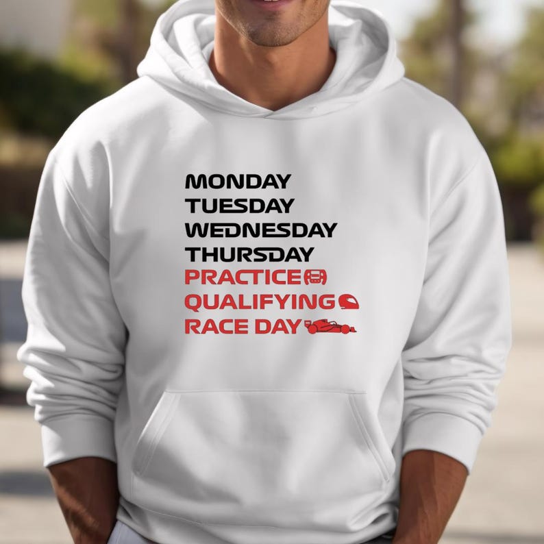Puede incluir: Sudadera con capucha blanca con un gr&aacute;fico frontal que enumera los d&iacute;as de la semana y t&eacute;rminos relacionados con las carreras en negro y rojo. El gr&aacute;fico incluye un coche de carreras y un icono de casco. La sudadera tiene un bolsillo delantero y una capucha.