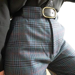 May include: Close-up of a pair of plaid pants in shades of blue, green, and red. The pants are worn with a black belt with a gold buckle. The pants are part of a vintage clothing collection.