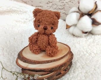 Può includere: Un piccolo orsacchiotto di peluche marrone seduto su una pila di rotonde di legno. L'orso ha occhi neri e un naso marrone. Le rotonde di legno sono disposte in una pila di quattro, con la rotonde superiore che è la più grande.