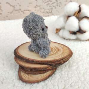 K&ouml;nnte beinhalten: Ein kleiner grauer Teddyb&auml;r sitzt auf einem Stapel aus Holzscheiben. Die Scheiben sind kreisf&ouml;rmig angeordnet und haben eine nat&uuml;rliche Holzoptik.