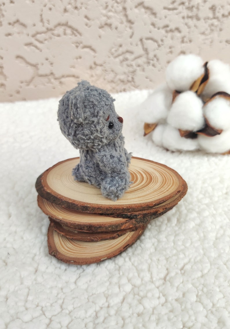 K&ouml;nnte beinhalten: Ein kleiner grauer Teddyb&auml;r sitzt auf einem Stapel aus Holzscheiben. Die Scheiben sind kreisf&ouml;rmig angeordnet und haben eine nat&uuml;rliche Holzoptik.