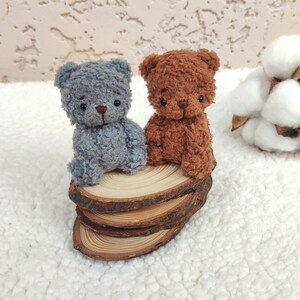 K&ouml;nnte beinhalten: Zwei kleine Pl&uuml;schb&auml;ren, einer grau und einer braun, sitzen auf einem Stapel Holzscheiben. Die B&auml;ren haben schwarze Augen und Nasen.