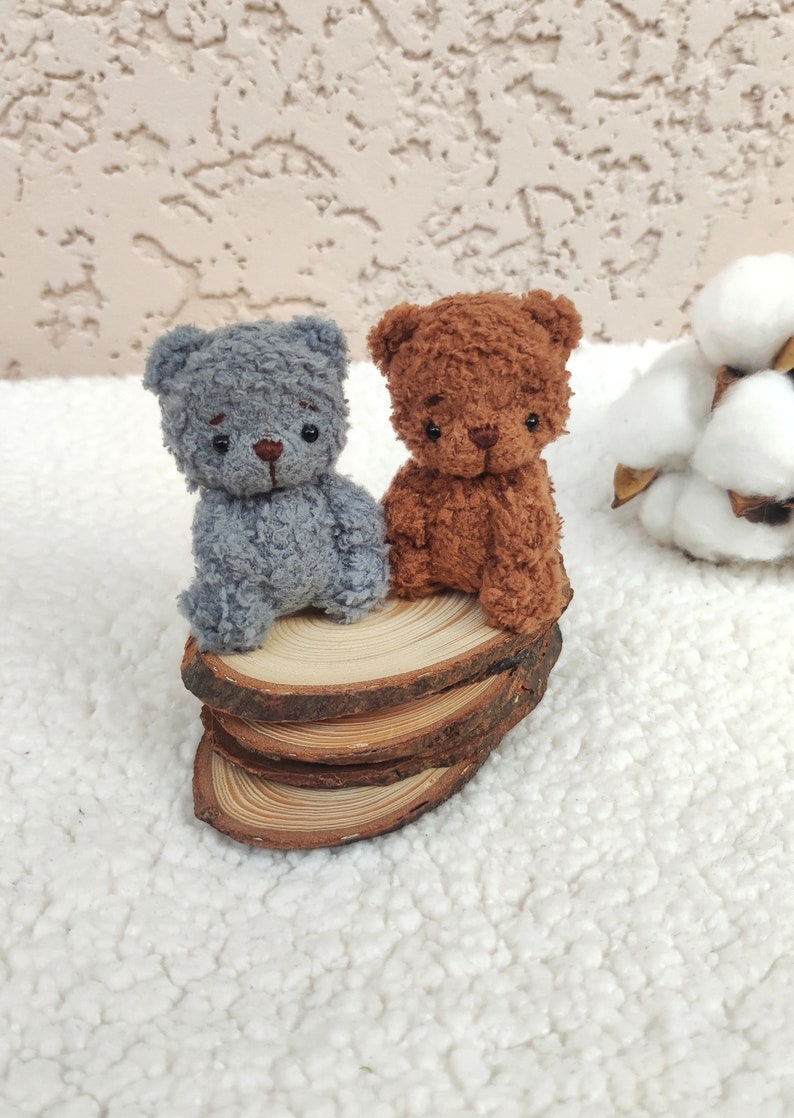 K&ouml;nnte beinhalten: Zwei kleine Pl&uuml;schb&auml;ren, einer grau und einer braun, sitzen auf einem Stapel Holzscheiben. Die B&auml;ren haben schwarze Augen und Nasen.