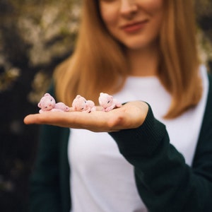 May include: A woman's hand holding four small pink crocheted bears. The bears are lying on their sides with their heads resting on their paws.