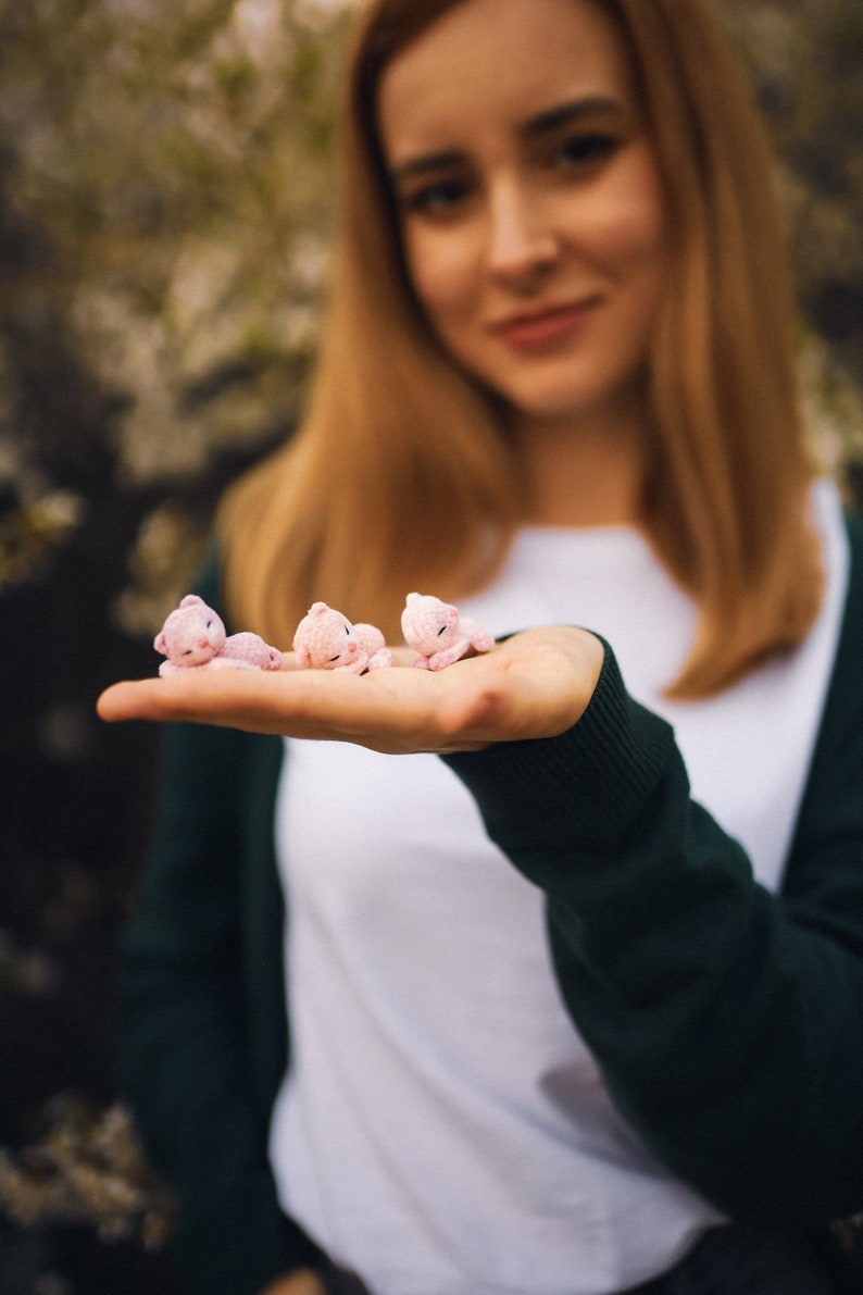 May include: A woman's hand holding four small pink crocheted bears. The bears are lying on their sides with their heads resting on their paws.