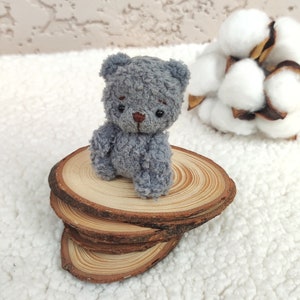 K&ouml;nnte beinhalten: Ein kleiner grauer Teddyb&auml;r sitzt auf einem Stapel aus Holzscheiben. Der B&auml;r hat eine braune Nase und schwarze Augen. Die Holzscheiben sind in einem Stapel von drei angeordnet.