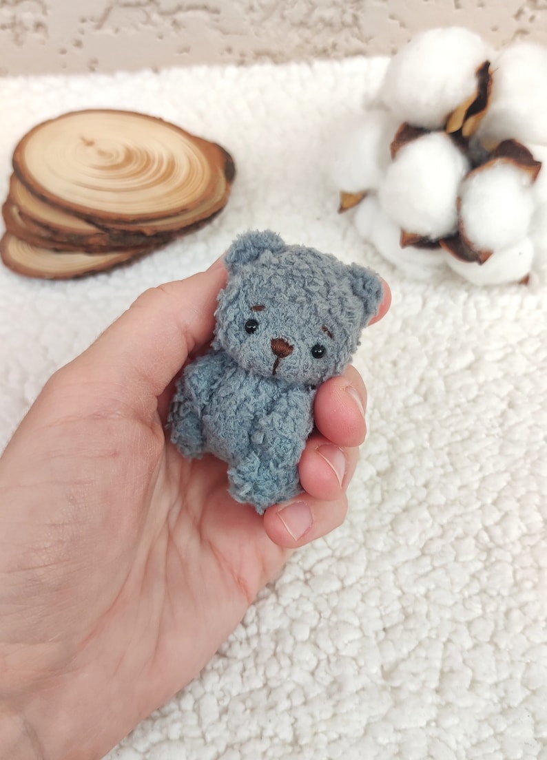 K&ouml;nnte beinhalten: Ein kleiner, grauer Pl&uuml;schteddyb&auml;r mit gestickten Augen und einer braunen Nase. Der B&auml;r wird in der Hand einer Person gehalten.