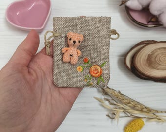 Mini plush teddy bear in pouch with embroidery. Cute stuffed tiny pocket animal