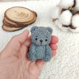 K&ouml;nnte beinhalten: Ein kleiner grauer Teddyb&auml;r mit schwarzen Augen und einer braunen Nase. Der B&auml;r sitzt in der Handfl&auml;che.