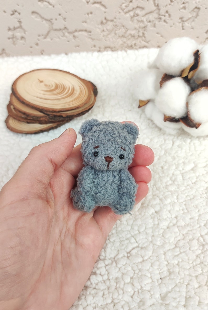 K&ouml;nnte beinhalten: Ein kleiner grauer Teddyb&auml;r mit schwarzen Augen und einer braunen Nase. Der B&auml;r sitzt in der Handfl&auml;che.