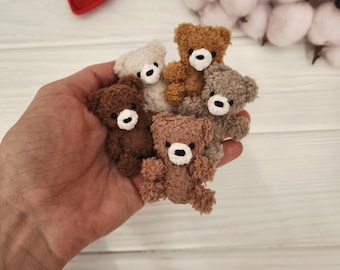 May include: A collection of small, handmade teddy bears in various shades of brown, beige, and gray. Each bear has a white muzzle and black eyes. The bears are made of a soft, textured material.