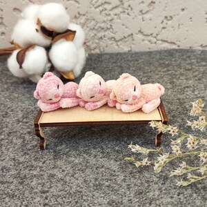 May include: Four pink crocheted kittens laying on a small wooden table. The kittens are facing the same direction and have black eyes and noses.