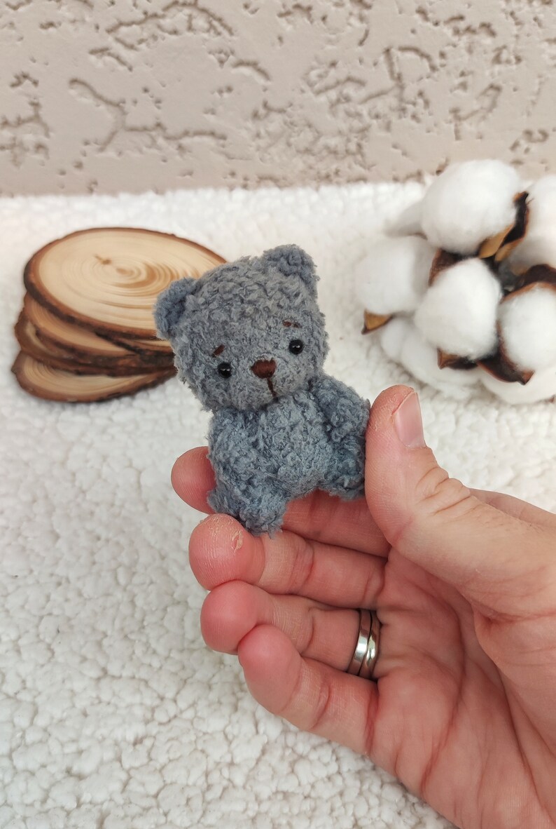 K&ouml;nnte beinhalten: Ein kleiner grauer Teddyb&auml;r mit schwarzen Augen und einer braunen Nase. Der B&auml;r sitzt in der Handfl&auml;che.