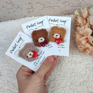 May include: Three small brown teddy bear pocket hug keychains with red hearts and embroidered messages. The messages read "When I can't be there to let you know I care", "Be there I care", and "F be there ow I care".