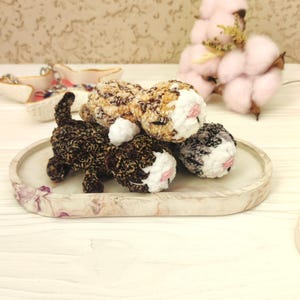 May include: Three crocheted cat toys in brown, black and white, lying on a white and purple marble tray. The toys are stacked on top of each other.