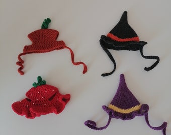 May include: Four small, handmade crochet hats including a red pumpkin-shaped hat with a green stem, a red strawberry-shaped hat with white dots, a black witch hat with an orange band, and a purple witch hat with a yellow band, all with ties.