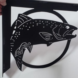 May include: Black metal wall mount bracket featuring a silhouette of a fish jumping out of a circle. The bracket is designed for hanging items on a wall.