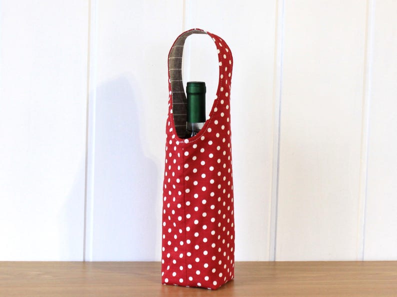 May include: Red wine bottle carrier with white polka dots. The carrier has a handle and is made of fabric.