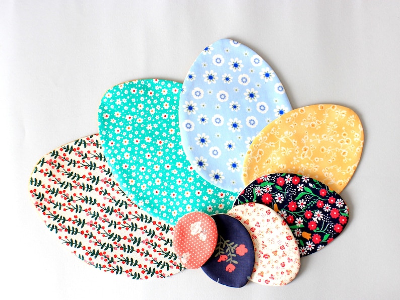 Puede incluir: Un conjunto de siete posavasos de tela con forma de huevo en varios patrones florales, incluyendo azul, amarillo, verde, rojo y blanco.