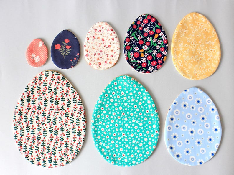 Puede incluir: Siete huevos de Pascua de tela en varios patrones y colores. Los huevos est&aacute;n hechos de tela y tienen una variedad de dise&ntilde;os florales y geom&eacute;tricos. Los huevos est&aacute;n dispuestos en un semic&iacute;rculo sobre un fondo gris claro.