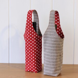 May include: Two fabric wine bottle carriers. One is red with white polka dots and the other is gray with white stripes.