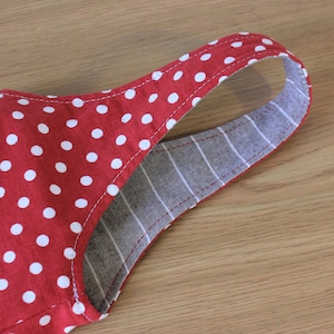 May include: Red and white polka dot fabric with a gray and white striped fabric sewn to the back. The fabric is folded over to create a strap.