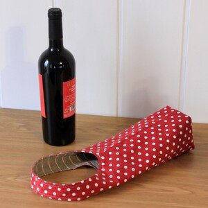May include: Red and white polka dot wine bottle carrier. The carrier is made of fabric and has a handle.