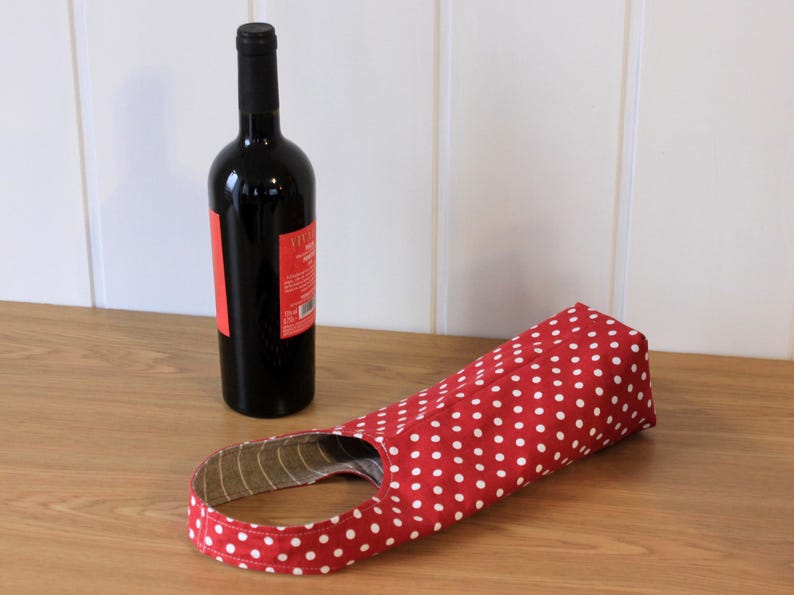 May include: Red and white polka dot wine bottle carrier. The carrier is made of fabric and has a handle.