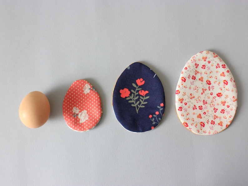 Puede incluir: Cuatro huevos de Pascua cubiertos de tela, un huevo marr&oacute;n liso y tres huevos estampados. Los huevos estampados son de lunares rojos y blancos, azules con flores blancas y blancos con flores rojas y naranjas.